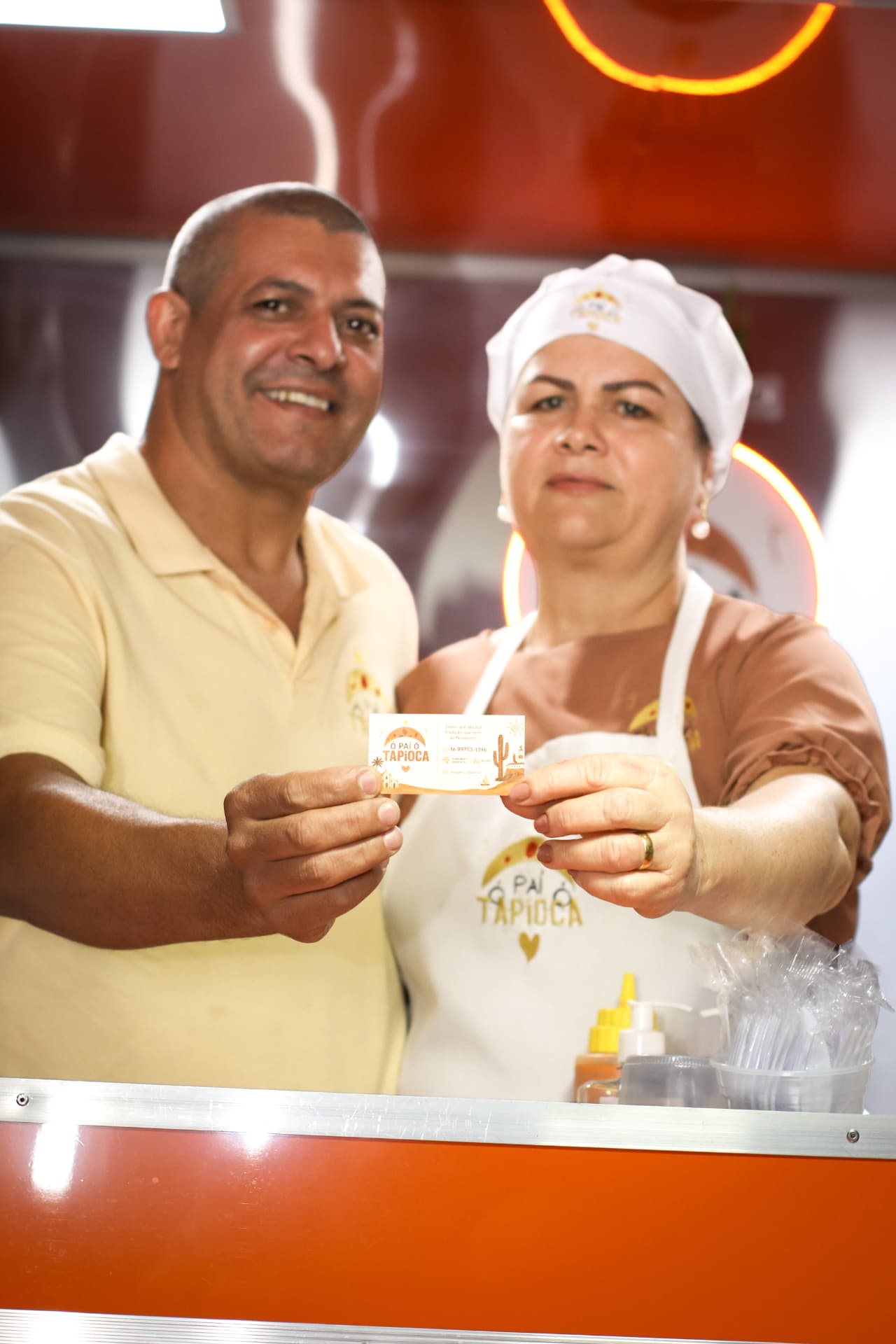 Equipe do Ó Paí Ó sorrindo no balcão do trailer com o cartão da casa